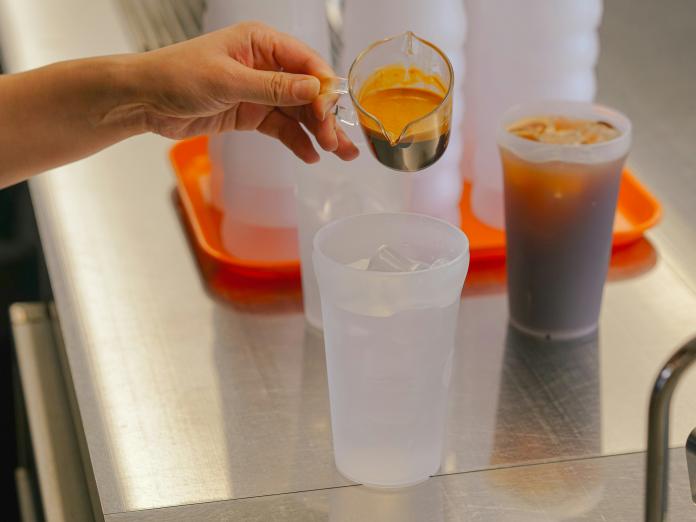 Photo shows a hand pouring coffee into a reusable cup